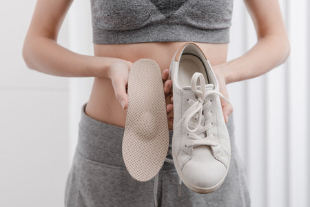 Woman putting orthopedic insole into shoe at home. Sports girl fitting orthopedic insole indoors, close up. Foot care banner. Flat Feet Correction. Treatment and prevention of foot diseases.の写真素材