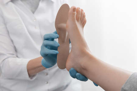 Doctor hands hold an orthopedic insole. Orthopedist tests the medical device. Orthopedic insoles on a white background. Foot care, comfort for the feet. Prevention of flat feet and foot diseases.の写真素材