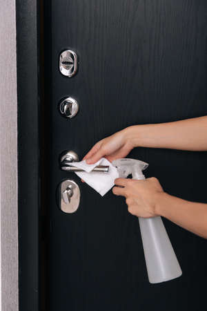 Cleaning black door handles with an antiseptic wet wipe. Woman hand using towel for cleaning home room door link. Sanitize surfaces prevention in hospital and public spaces against corona virusの写真素材