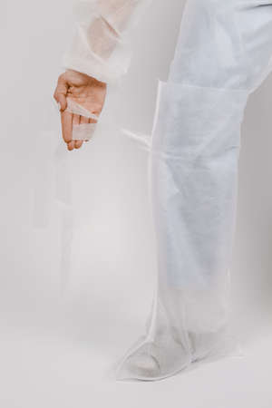 Nurse wears disposable gown and disposable shoes cover. Doctor putting on white medical shoe covers, closeup. Clothes for hospital visits or medical uniform concept. Overshoes protectionの写真素材