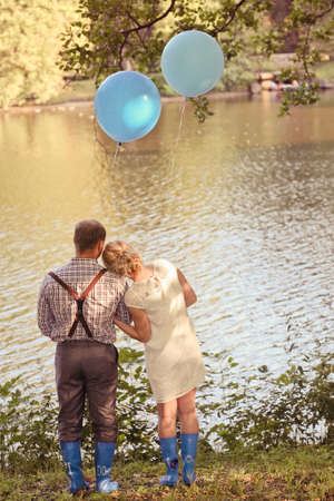 Young couple with balloons in their hands on the coast of the lake. Man and woman are in love. Concept for postcard or Valentines day. Two blue balloons with smiley facesの写真素材