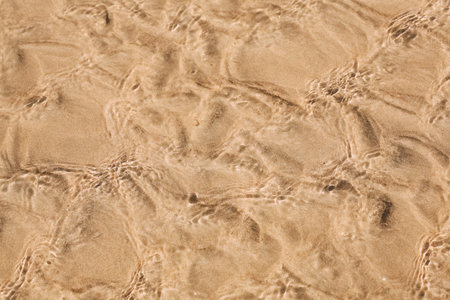 Sea waves and sun glare over the sandy coast. Sand texture background. Nature sand top view on beach...
