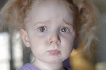 Close up portrait of a cute little redhead girl with a sad pouting expression and big sulky eyes looking straignt at the cameraの写真素材