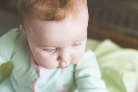 Close-up of cute baby looking down in crib with soft lightの写真素材