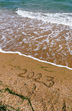 2023 written on the beach sand. Bright turquoise green sea waves with foam. Touristic concept for...