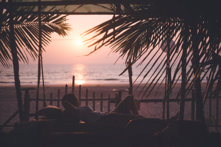 Silhouette of a person relaxing at a cafe and the setting sun on the main beach in Gokarna, Karnataka, Indiaの写真素材