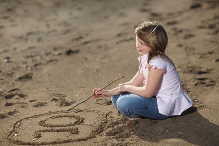 Blonde young girl on the beach writing the number ten in the sand, selective focus on writingの写真素材