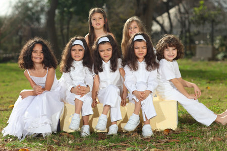 Seven happy young children including triplets with white clothes sitting on yellow cubes smiling, sun reflection in hair, backlight; shallow depth of fieldの写真素材