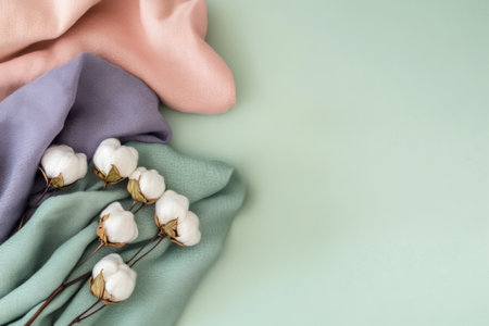 Flat lay of multicolored cotton fabrics and flowers on pastel green surface. Top view highlights natural fibers and gentle, sustainable aesthetic.の素材