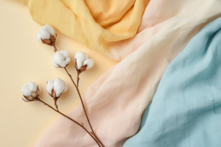 Flat lay of multicolored cotton fabrics and flowers on pastel beige surface. Top view highlights natural fibers and gentle, sustainable aesthetic.の素材