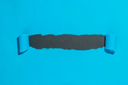 Blue paper opened ripped to reveal black copy space. Paper ripping into scrolls opening window in front of black surface to make space for your important messages. Torn blue paper.の写真素材