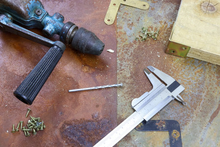 Caliper old vintage drill bit screws woodwork on rusty table. Hand vintage drill and caliper on rusty metal background, tools for repairの写真素材