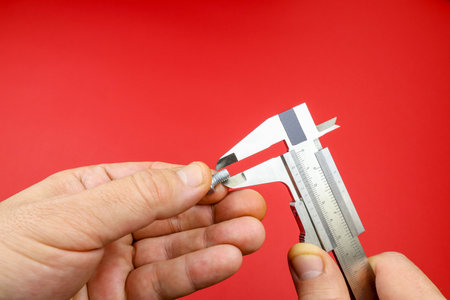 Hands measuring caliper screw workshop. Man hand holding vernier caliper on red background, closeupの写真素材