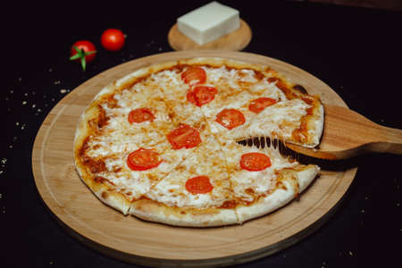 Appetizing pizza with cheese and tomatoes. A slice of pizza with melted cheese. Pizza on a wooden spatula.の写真素材