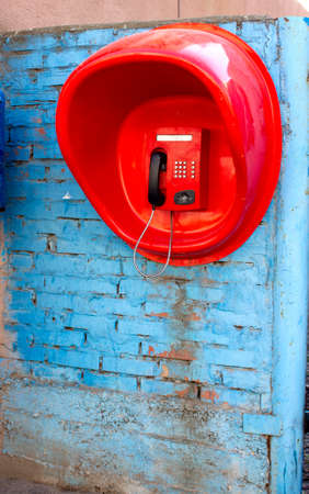 street payphone telephone set in a red booth on the wall close-upの写真素材