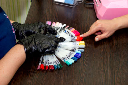 girl chooses color of nail polish for manicure in beauty salon using plastic samplesの写真素材