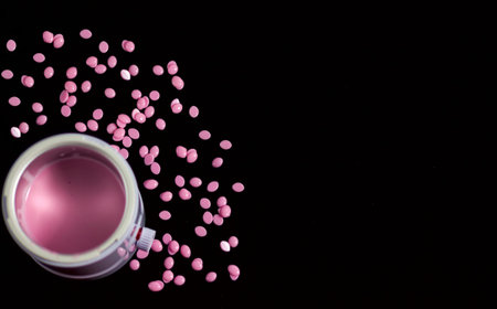 an electric appliance waxclave with molten pink wax inside during operation and wax in granules scattered around on a black background is used for cosmetic purposes to remove hair depilationの写真素材