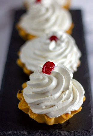 many festive cakes with whipped cream stand in a row on the table on a green background close up
