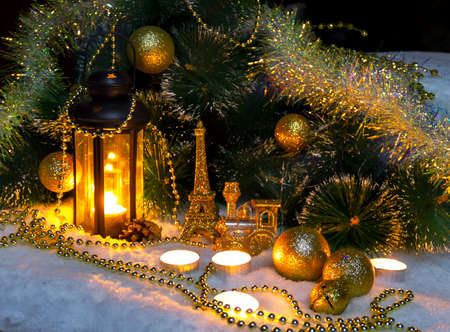 Christmas decor vintage lantern with a candle shines next to decorated pine branches with Christmas tree golden toys on the snowの写真素材