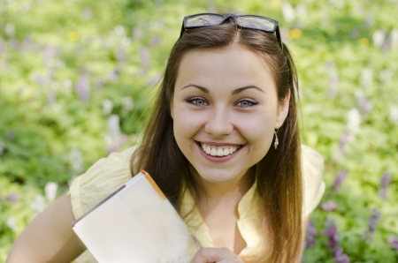 Portrait of beautiful smiling girl with book and glasses in spring forestの写真素材