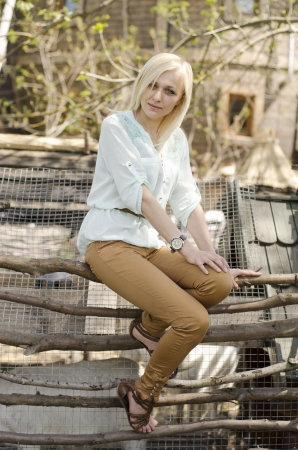 Portrait of beautiful blonde girl sitting on wood fenceの写真素材