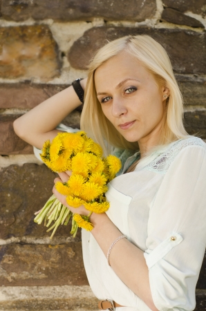 Portrait of beautiful blonde girl with bouquet of dandelion on stone backgroundの写真素材