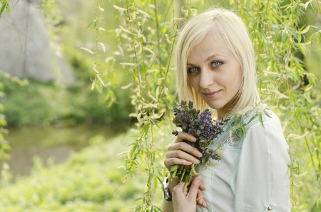 Portrait of beautiful blonde girl with lungwort flowers on willow tree backgroundの写真素材