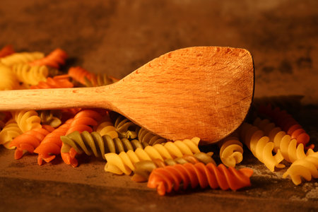 Three-colored pasta with cooking spoon on stone backgroundの写真素材