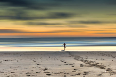 A child runs toward the sea at sunset in a loneliness beachの写真素材
