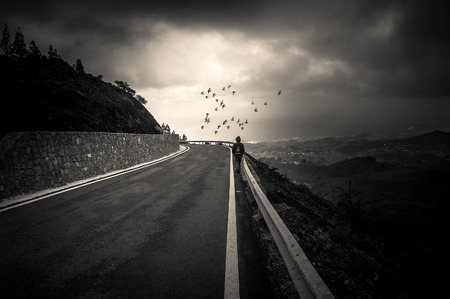 A boy walks down a lonely road toward a light horizonの写真素材