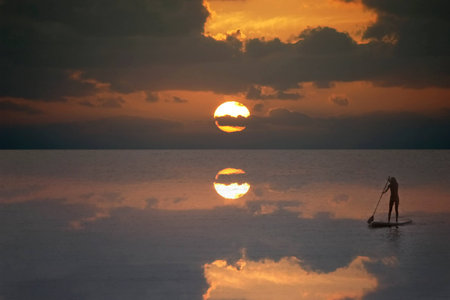 Silhouette of a stand-up paddle surfer (standup paddleboarding surfer) girl in the sea in a...