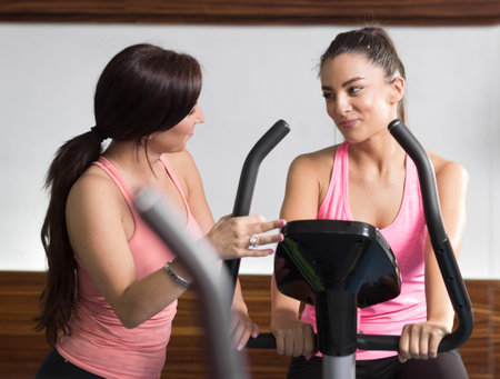 Two women gym, upper body shot, instructor talking listening bike sitting standing.の写真素材
