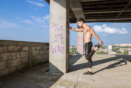 young man fit abs muscular stretching leg outdoors sunny shirtless construction building