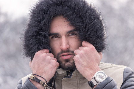 one young adult man cold winter outdoors head face closeup. looking at camera, warm clothes. serious expressionの写真素材