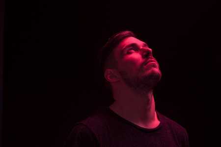 one young adult man, looking above, looking up, red color light, black background