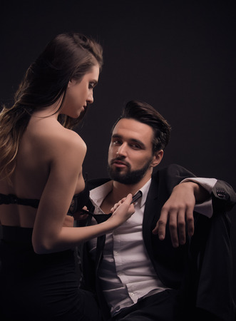 two people, young adult  couple woman pulling man tie dark, black backgroundの写真素材