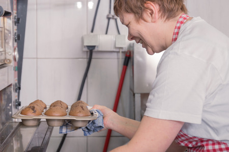 happy smiling one mature woman cooking closeup woman oven finished done muffins, side view, commercial kitchenの写真素材