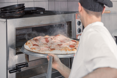 one young adult man chef closeup oven chef pizza steam, commercial kitchenの写真素材