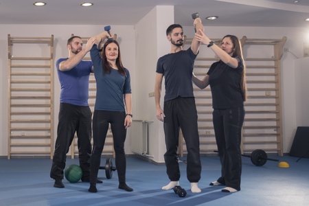 four young people group, two instructor, two trainer, showing learning educating fitness training exercise dumbbells, arms raisedの写真素材