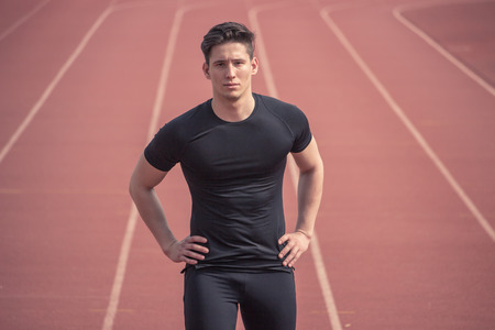 one young man, runner posing, red running tracks, outdoors, black clothes, fitness athlete, looking at cameraの写真素材