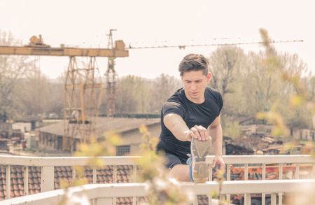 one young man, stretching leg on fence, outdoors industry treeの写真素材