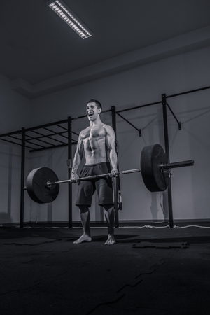 one young man only, bodybuilder deadlift, shouting screaming, weights bar barbell, dark gym indoors, black and white image.の写真素材
