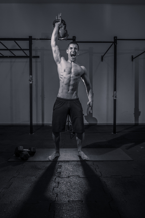 one young man bodybuilder, kettle bell, shouting screaming, dark gym indoors, black and white image.の写真素材