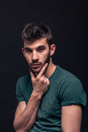 one young adult man only, handsome portrait, hand on beard, black backgroundの写真素材