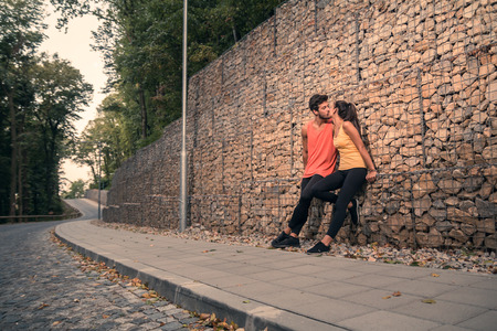 two young adult people, sitting rocks, outdoors nature forest asphalt, sport clothes, kissingの写真素材