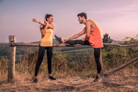 two young people, man woman, stretching legs arms, sports, fitness, outdoors, mountain, nature, sky, sunny dayの写真素材