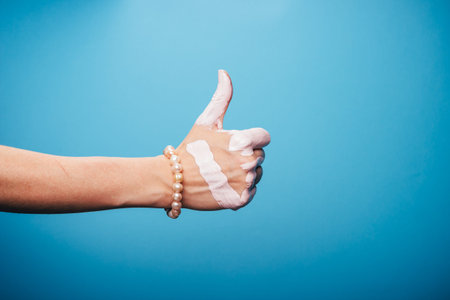 one woman hand, Caucasian painted white hand skin, blue background, jewelery bracelet, thumbs up gesturingの写真素材