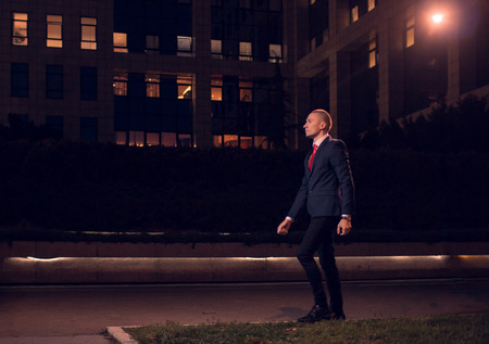 One young adult man walking businessman suit, formal wear, outdoors, night evening dark portrait, modern building exteriorの写真素材