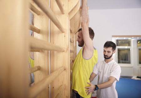 two young men, one man physiotherapist correcting patient back, exercising room.の写真素材