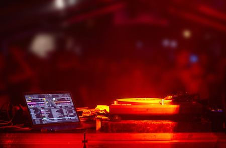 party backstage, dj booth equipment turntables computer, out of focus blured crowd, red lights.の写真素材